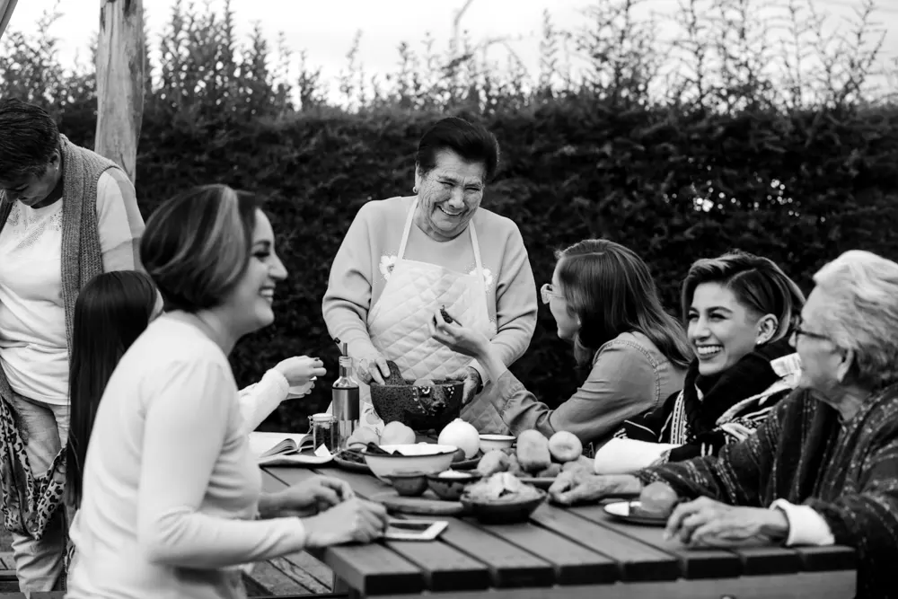 A group of women gathered around a picnic table, laughing together as they make homemade quacamole