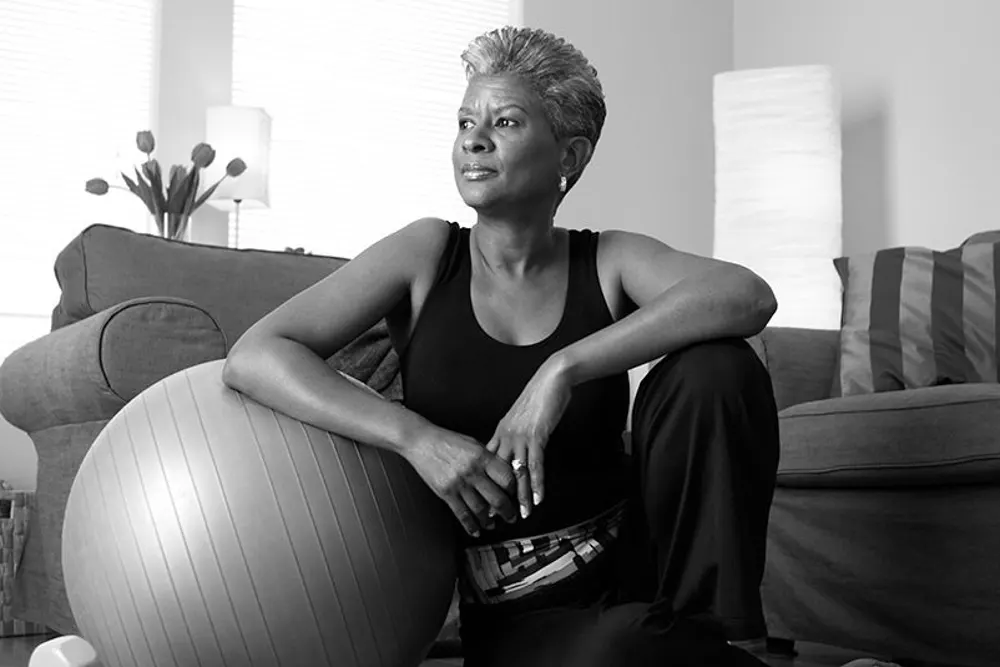 A woman sits on her living room floor, leaning on an exercise ball after completing her workout to keep her brain healthy
